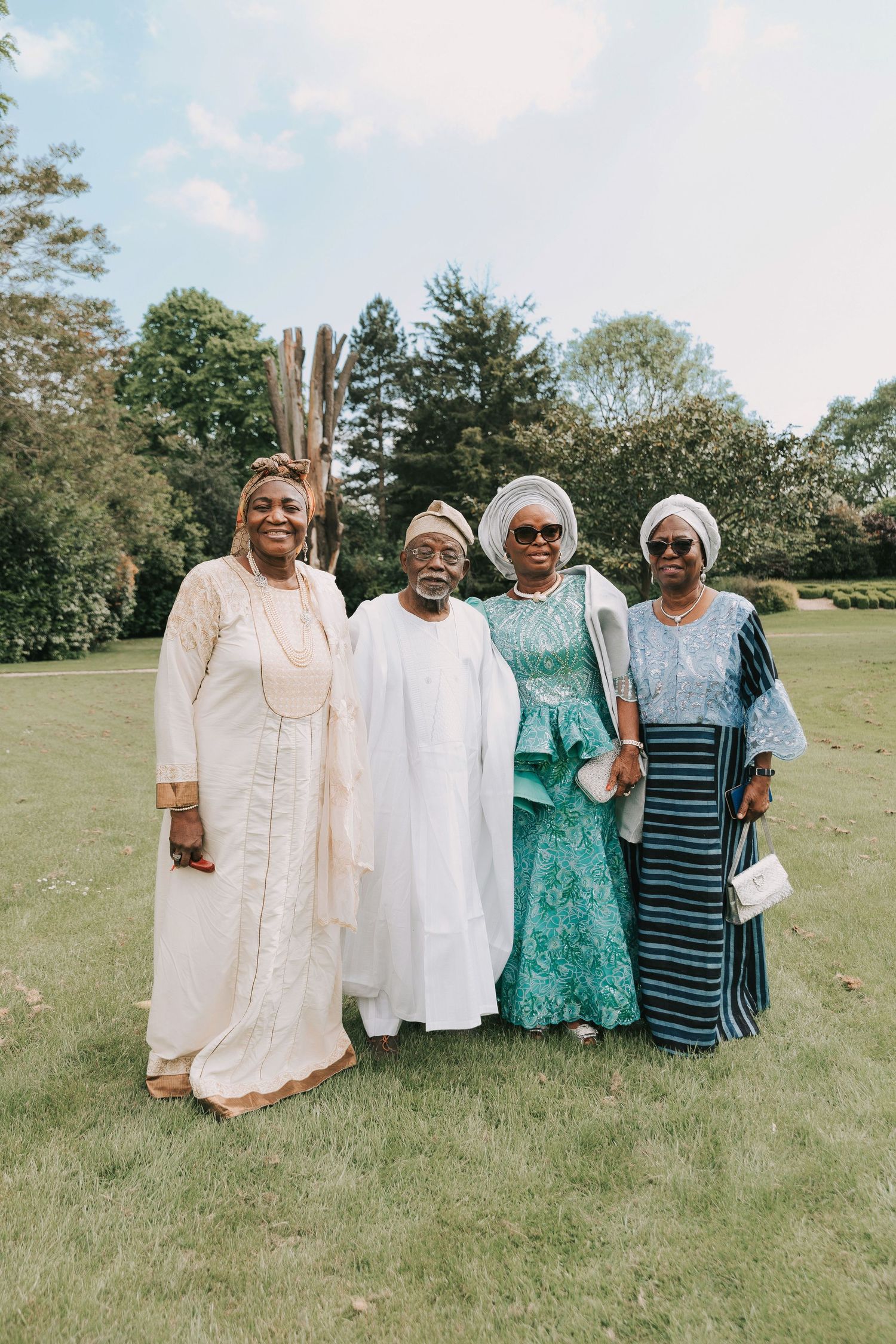 A group of people wearing traditional African-inspired attire pose together on a grassy lawn during a sunny day.