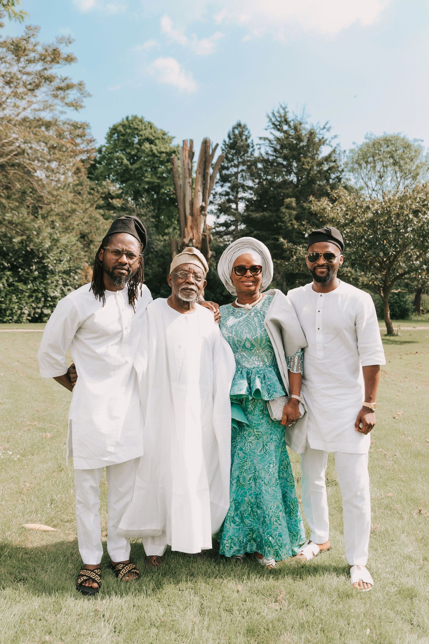 A group wearing coordinated white and green outfits poses together on a sunny grassy lawn.