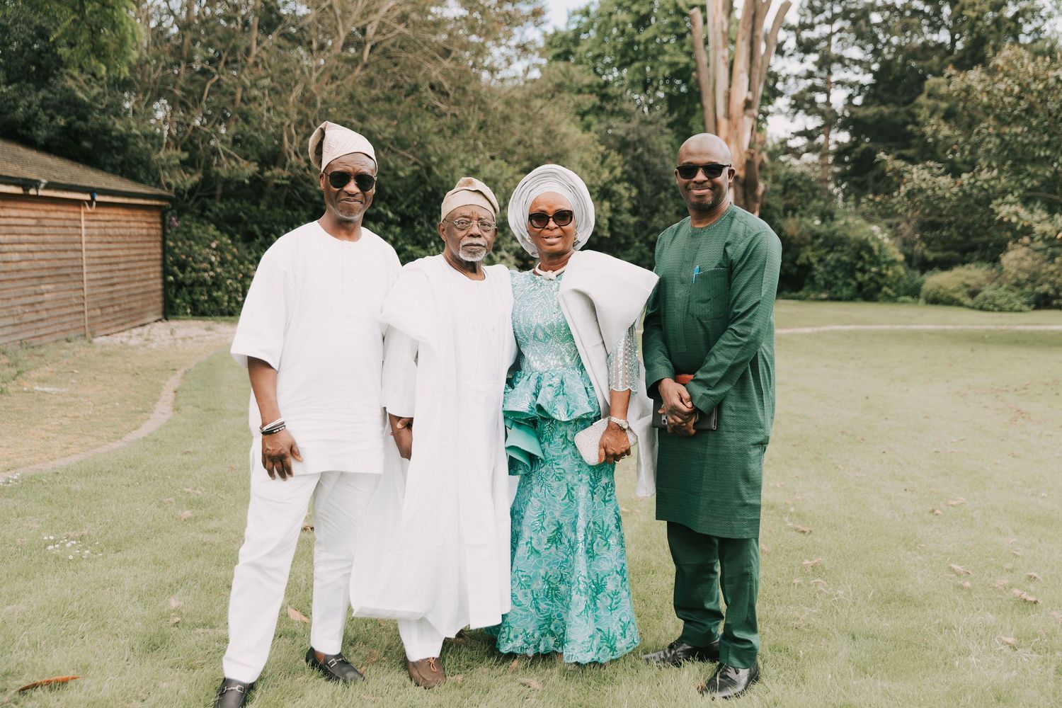 A group in white, green and cream colored traditional Nigerian clothing poses on Orsett hall landscaped lawn.