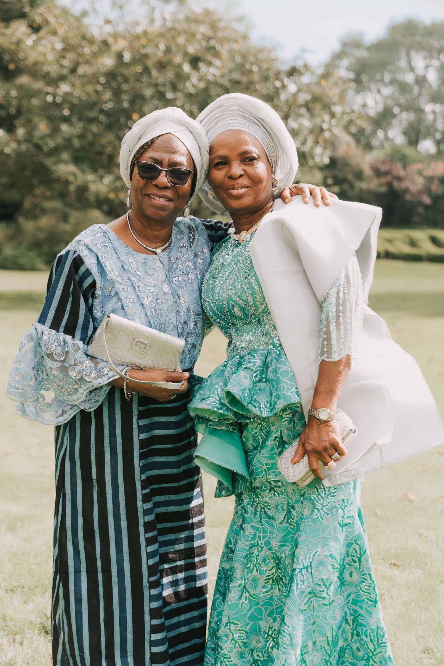 Two people in coordinating outfits embrace and smile while standing in a grassy outdoor setting.