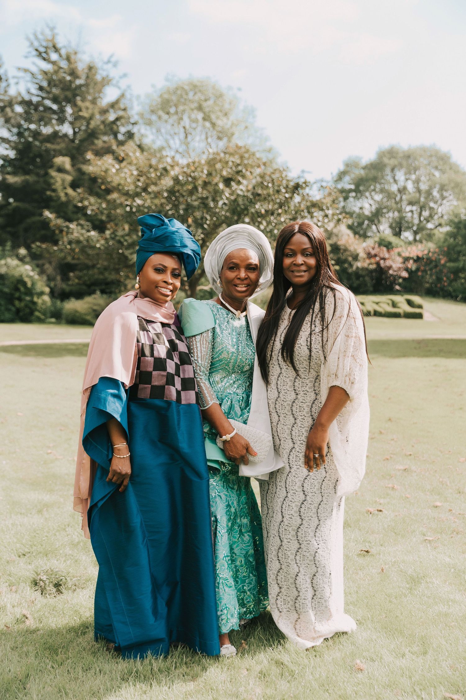 Three people wearing coordinated teal, green and white outfits pose together outdoors in a grassy field.