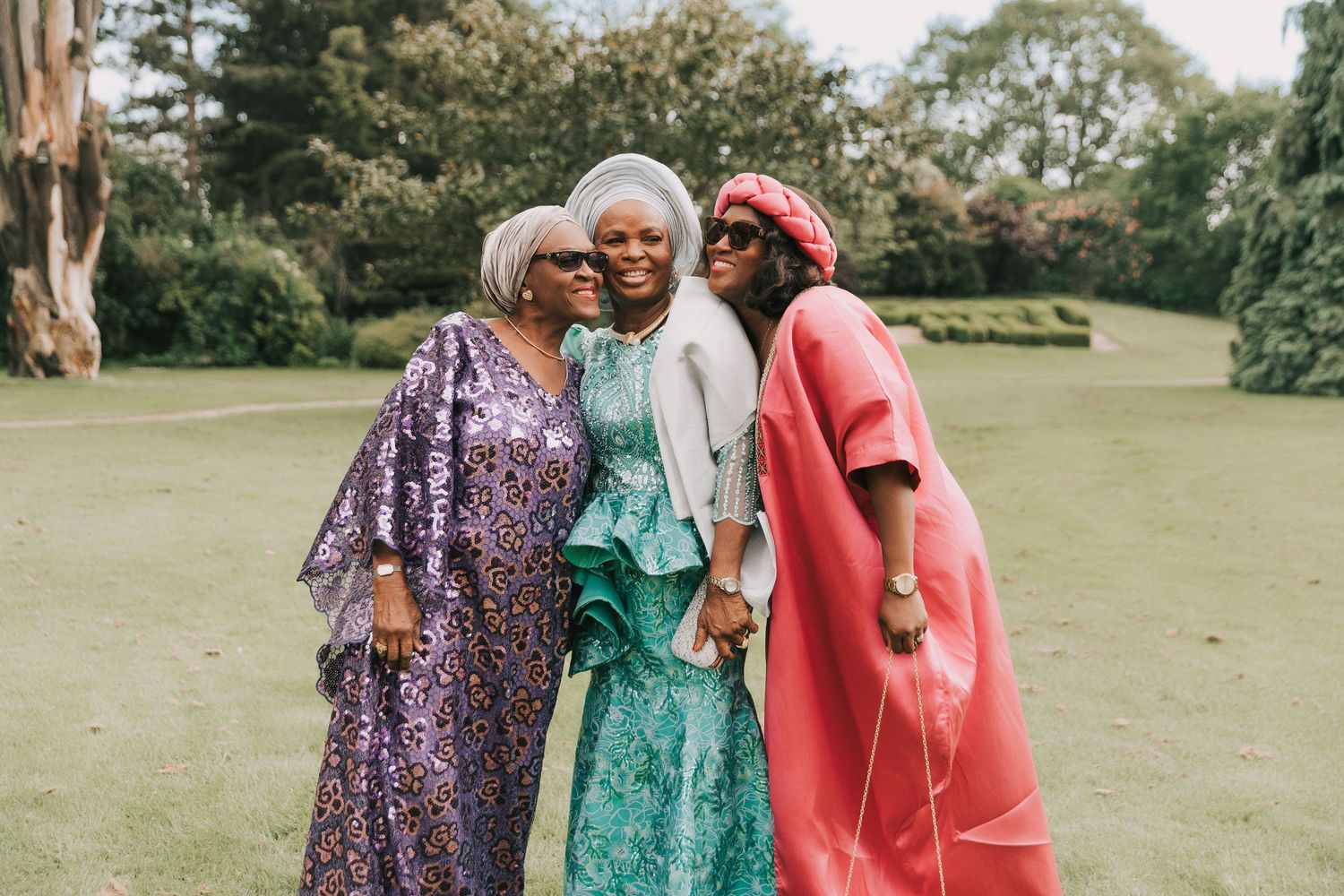 Three people in colorful dresses share a joyful moment outdoors on a sunny day.