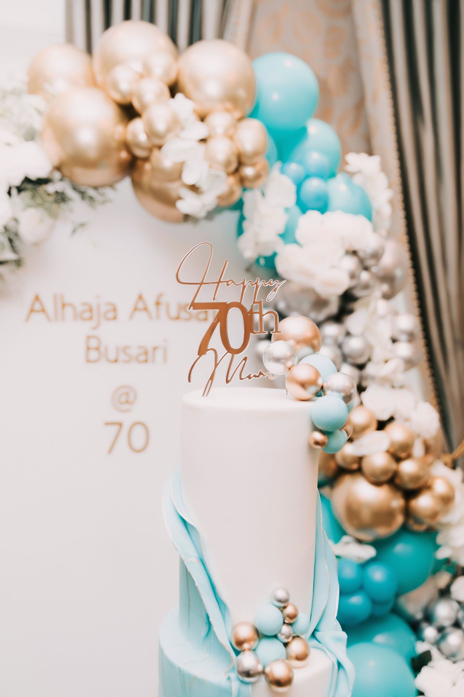Elegant party decor featuring balloon garlands in turquoise and gold with white accents against a striped wall.