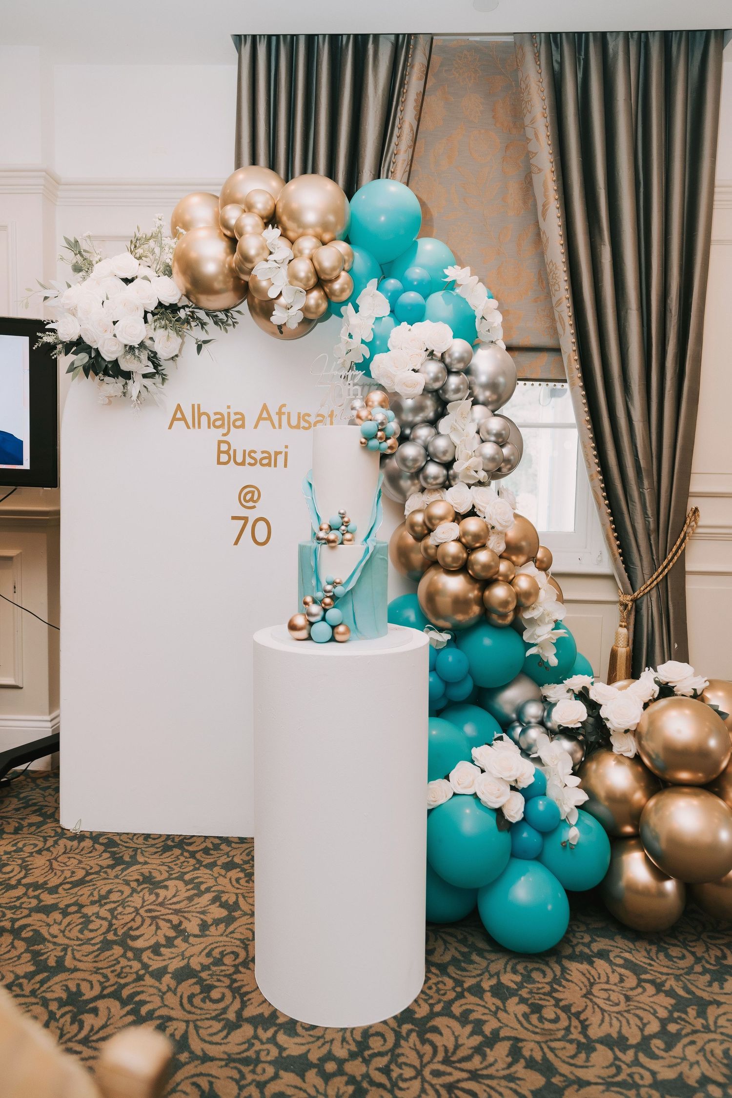 Balloon arch installation in teal, gold and white colors with event signage.