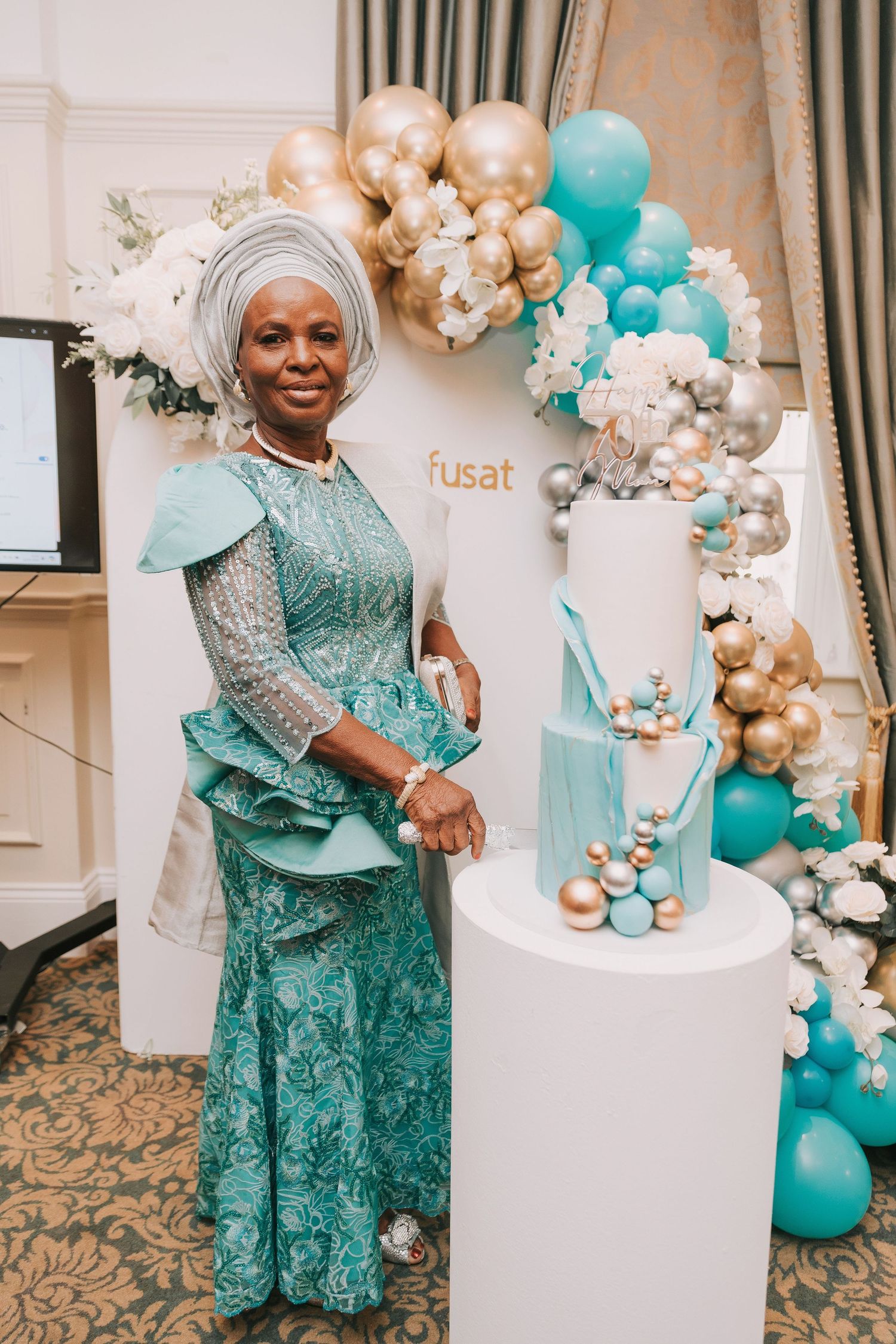 Celebration setup with teal and gold balloon arch, white cake, and elegant decor.