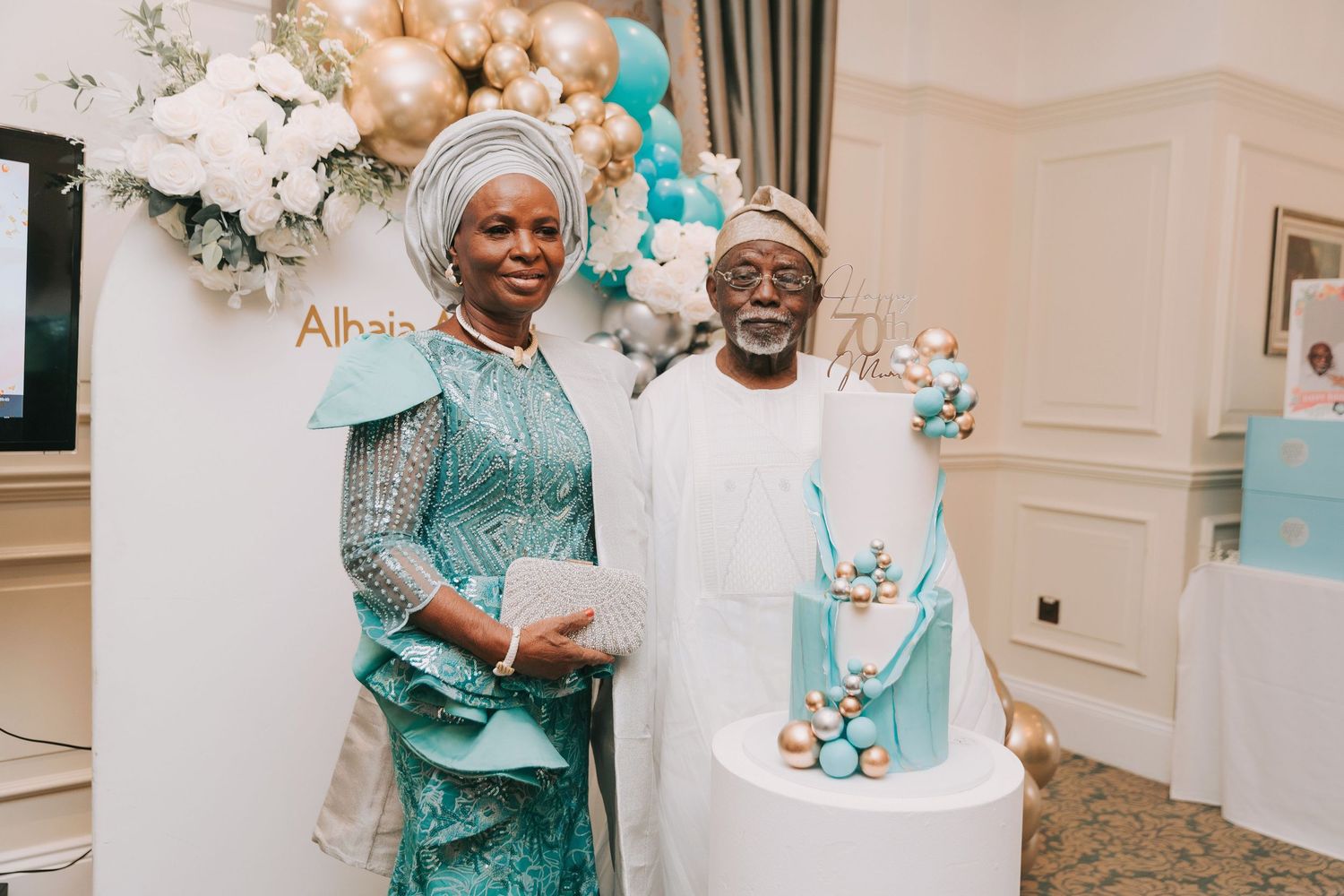 Celebration event featuring a turquoise and gold decorated cake with balloon arch and floral arrangements.