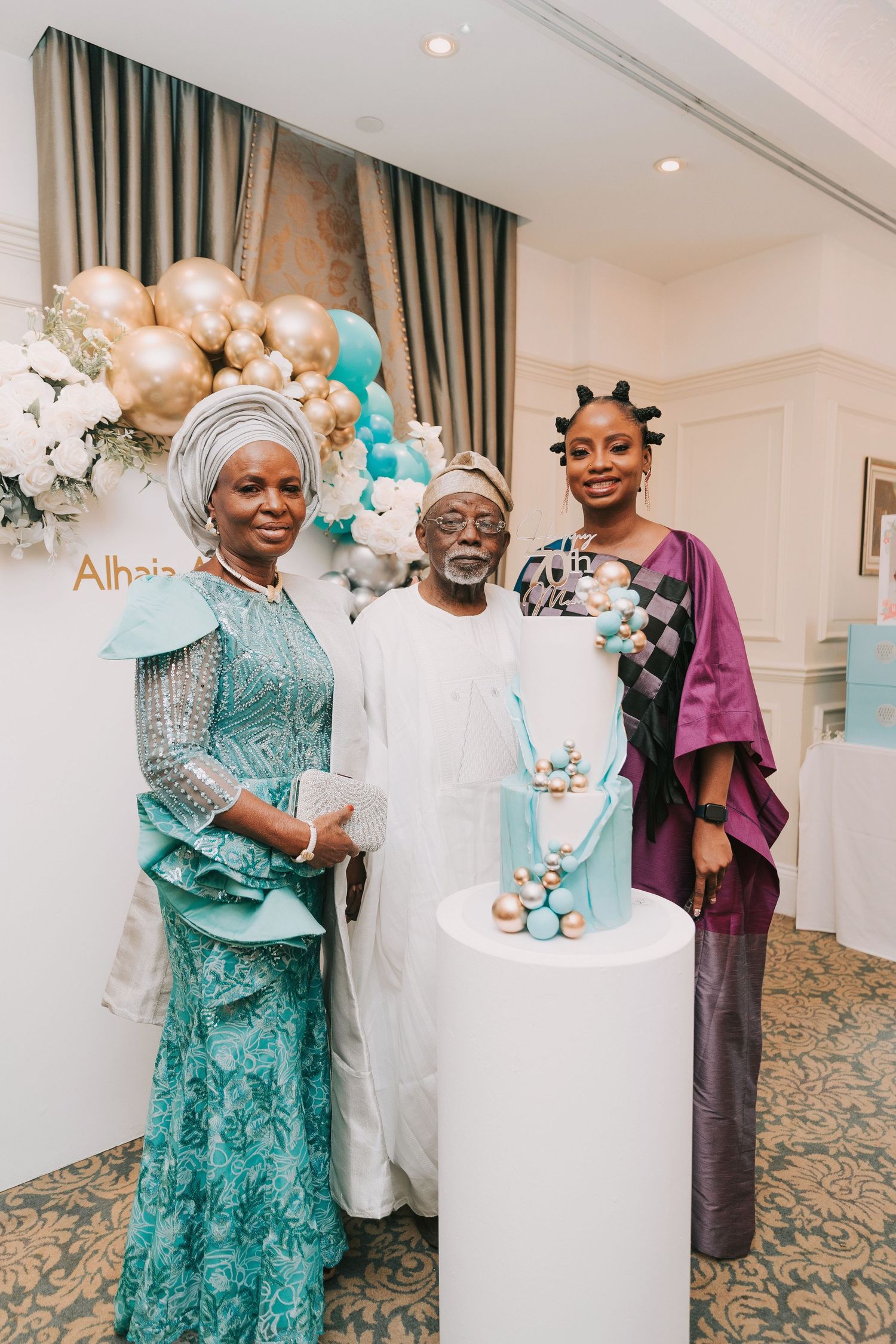 Elegant event setup with turquoise and gold balloon decorations and a tiered cake on display.