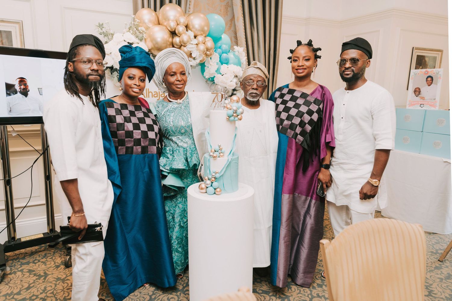Festive gathering with balloon decorations and a decorated cake display in turquoise and gold theme.