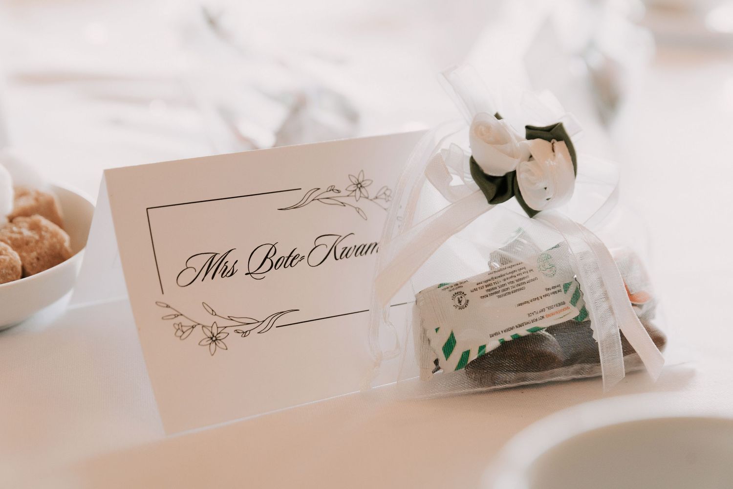 Elegant wedding place card and favor box with white ribbon displayed on white tablecloth at reception.