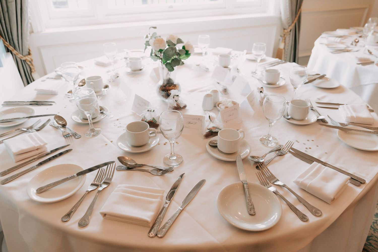 Formal table settings with white linens, fine china, and polished silverware at an upscale event.