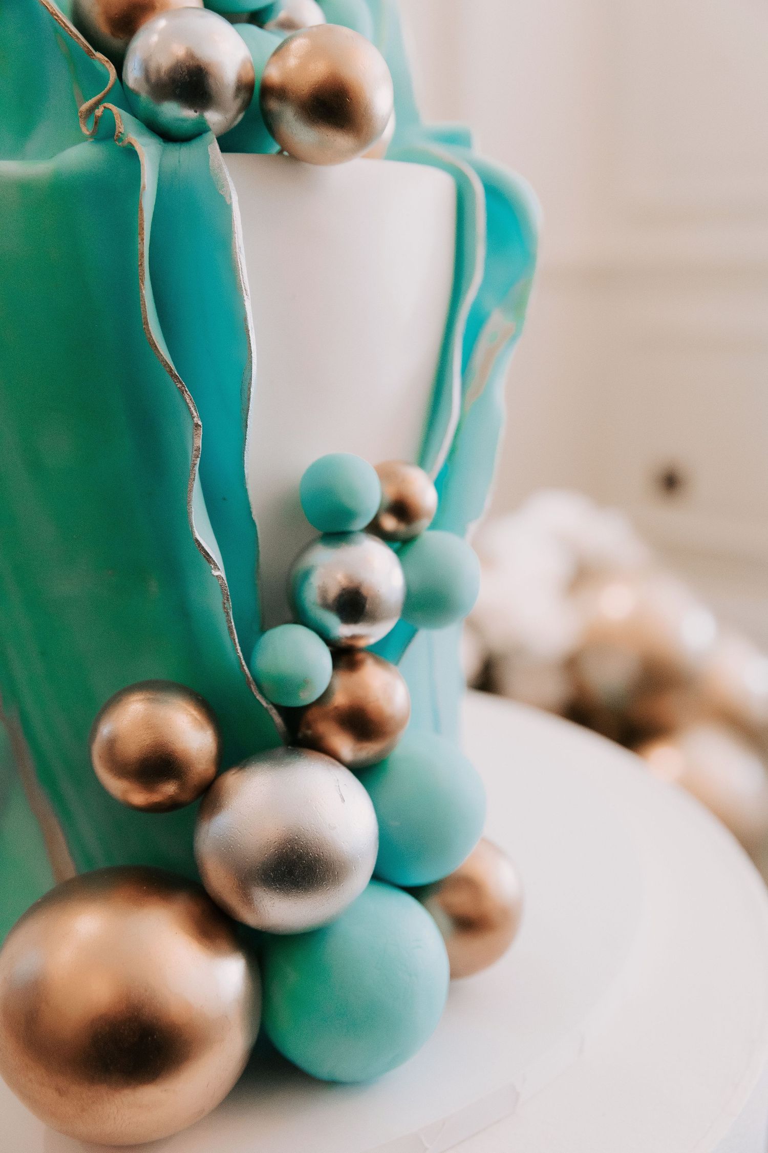 Close-up of modern cake decoration featuring teal and gold metallic spheres.