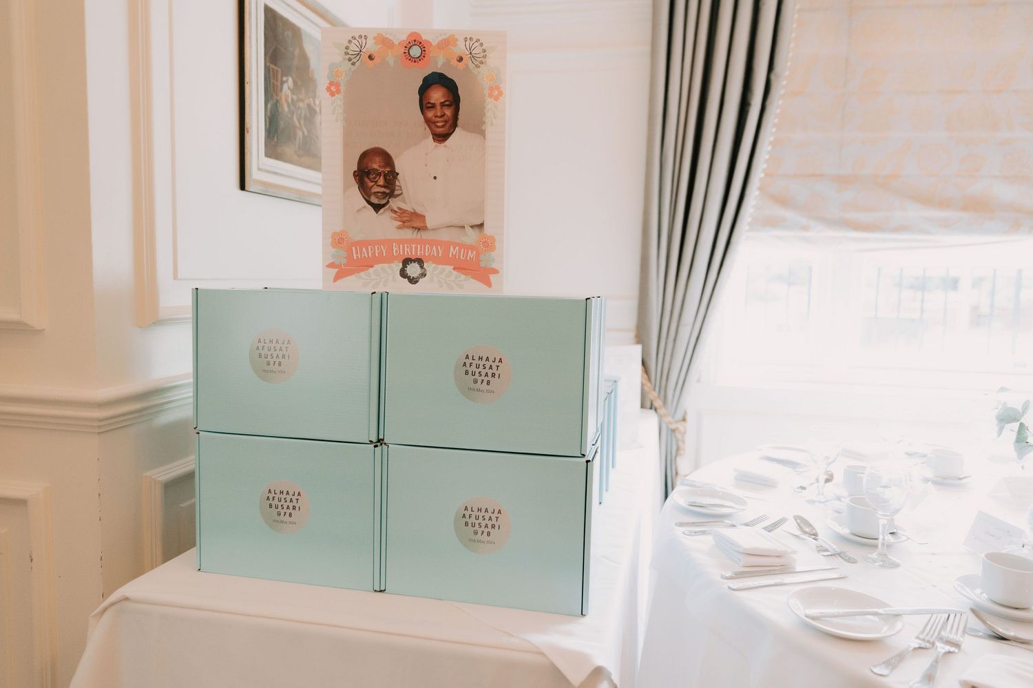 Mint green gift boxes stacked on a white table with a framed photo and curtains in the background.