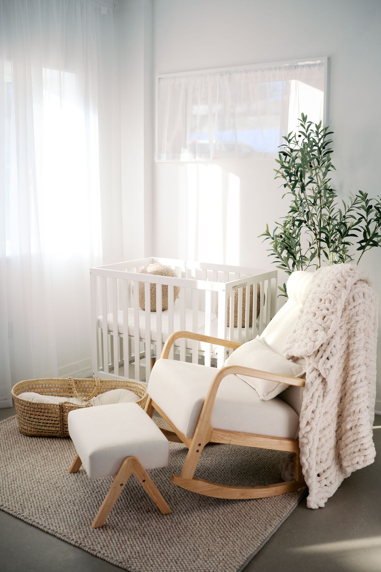 Modern living room corner with wooden lounge chair, white throw blanket, and potted plant on gray carpet.