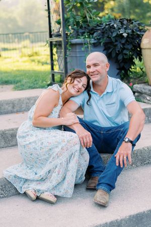 A couple sits close together on outdoor steps during a casual photo session in natural lighting.
