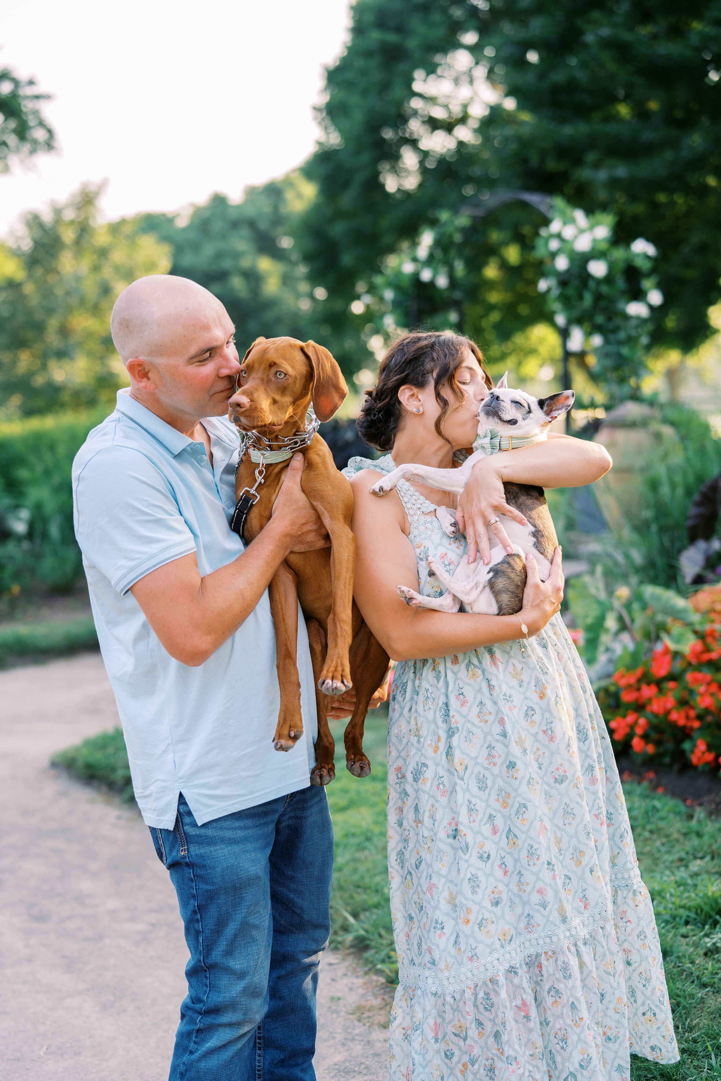 Couple plays with their brown dog while enjoying a sunny day in flowering garden.