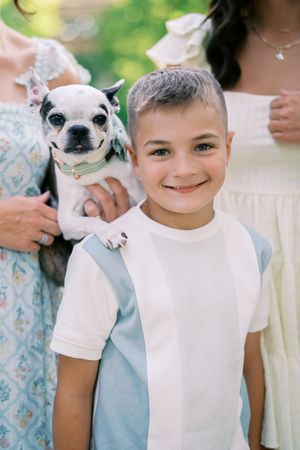 A small white Chihuahua puppy being held next to someone wearing a white shirt against a soft blurred background.