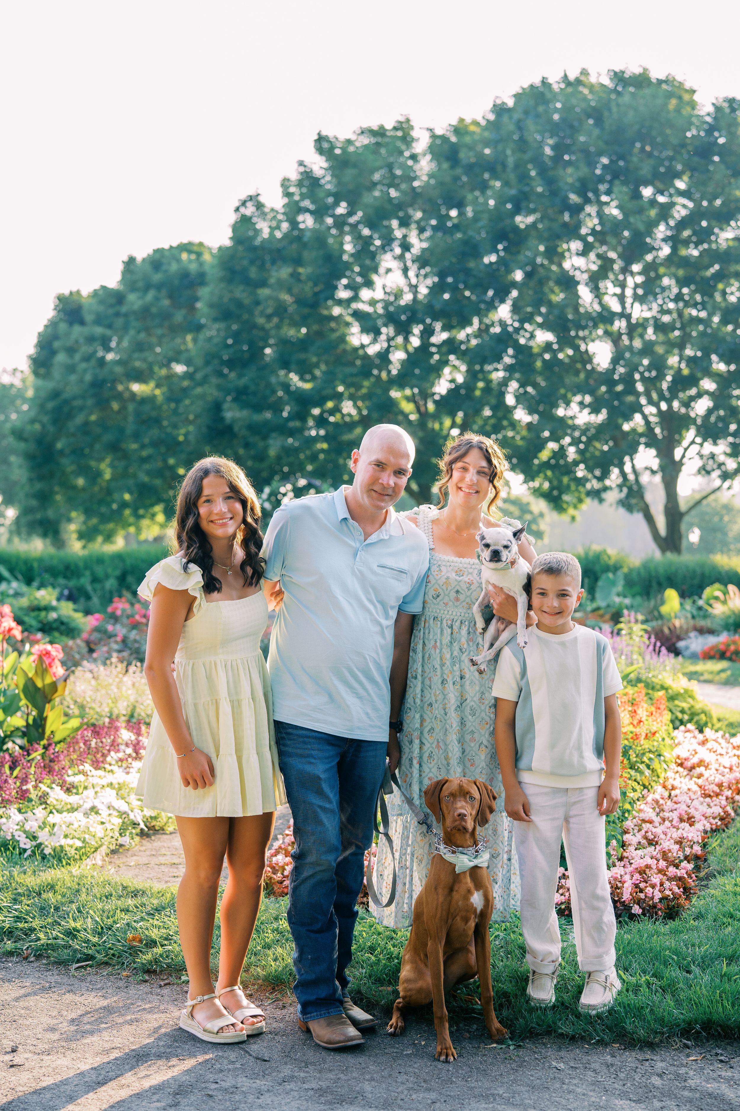 Family and their brown dog pose together in a beautiful garden setting with blooming flowers.