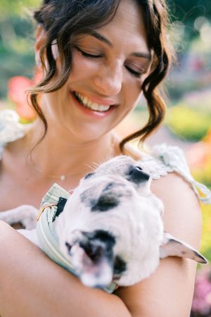 A small white and black spotted puppy being held and cuddled in an outdoor setting with soft natural lighting.
