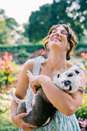 Woman shares joyful moments with her pet dog among colorful garden flowers.