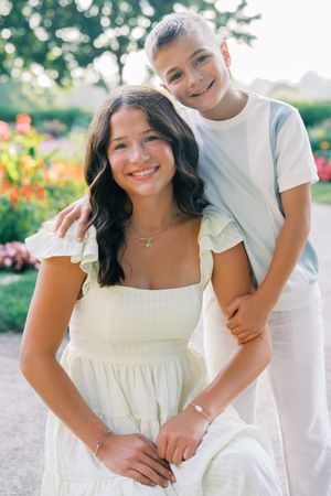 A pair in coordinating white outfits share a tender moment in a sunny garden setting.