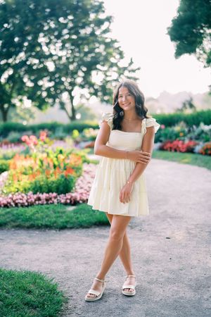 A yellow sundress flows gracefully as someone poses along a garden path with colorful flowers in the background.