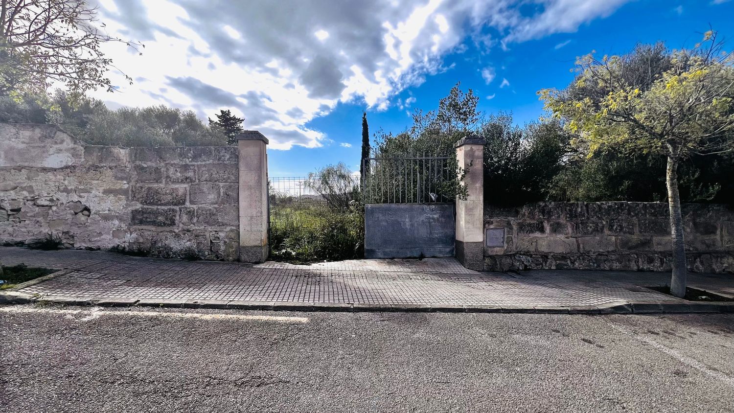 A stone gateway with ornate columns and a wrought iron gate, leading to a paved path.