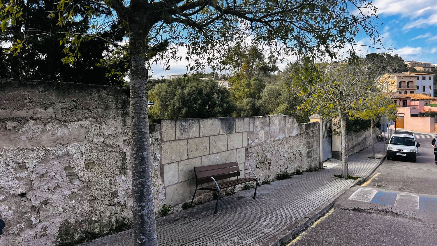 A stone wall and bench under a large tree in a scenic outdoor setting.
