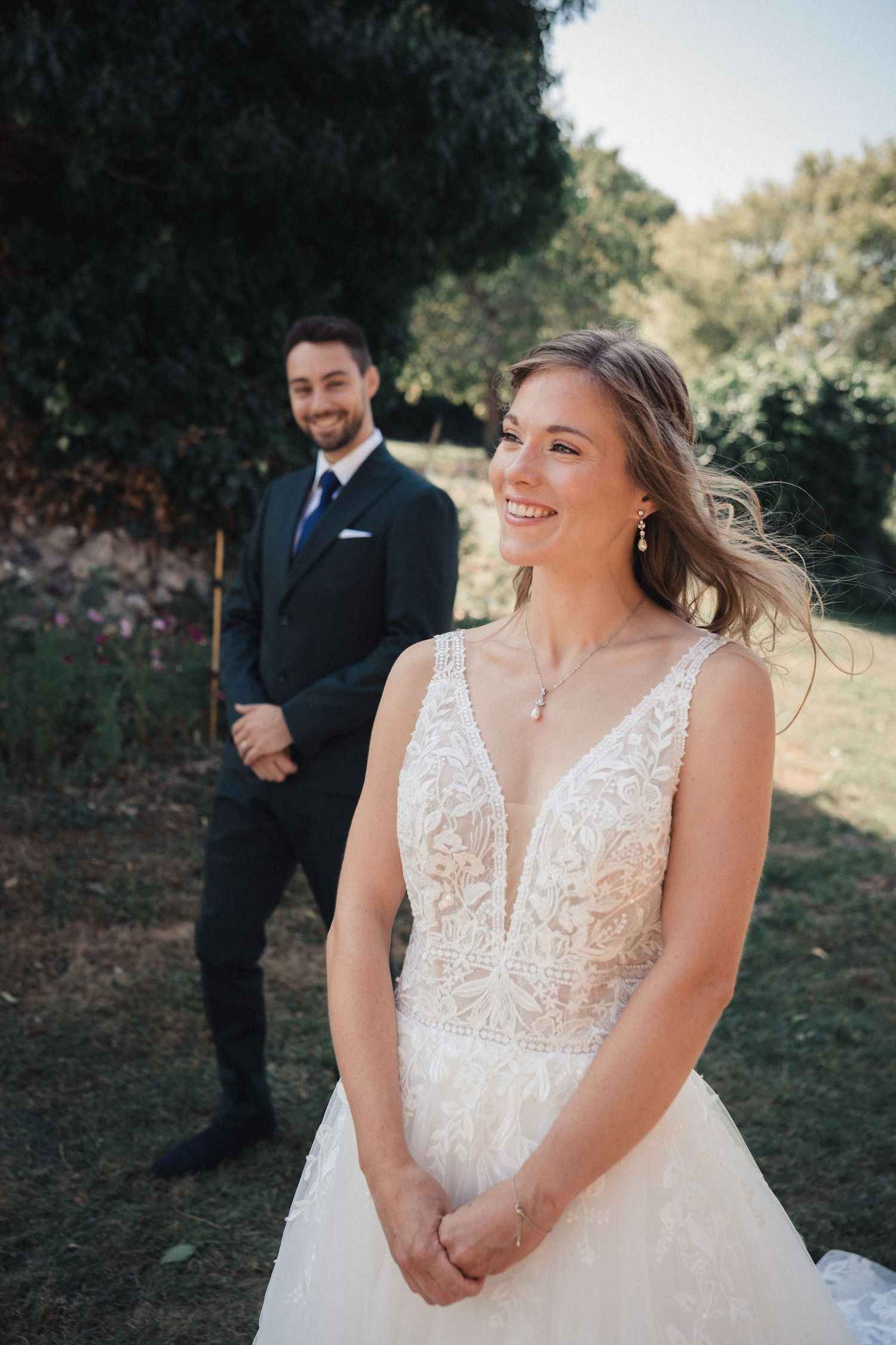 A bride in a white lace wedding dress smiles joyfully during an outdoor photo session.