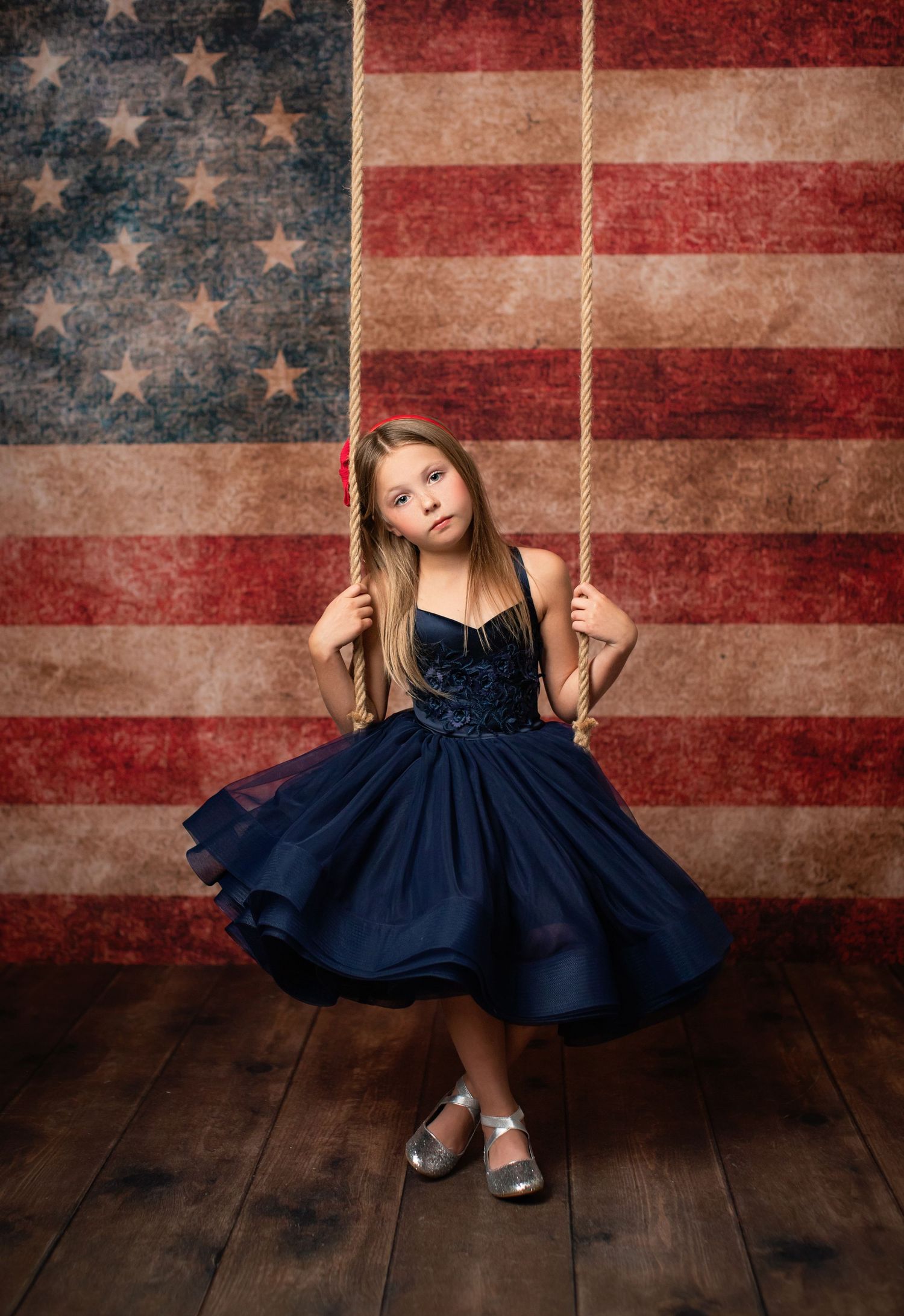 A navy blue dress twirls against a vintage American flag backdrop on rustic wooden floorboards.