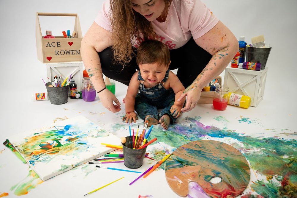Multiple hands create vibrant artwork with paint and art supplies on a white surface during a creative session.