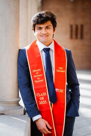Graduate in navy suit and red graduation stole smiles during outdoor photo session at USC.