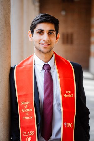 Graduate in black suit and red USC graduation stole with purple tie stands against neutral background.
