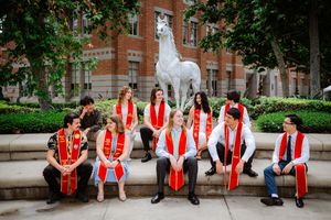 USC graduates in red sashes pose near the iconic Tommy Trojan horse statue on campus.