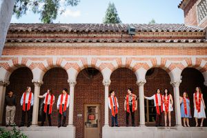 USC graduates in red stoles stand in arched brick colonnade during graduation photos.