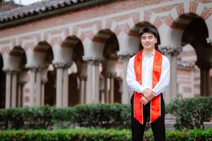 A person in academic regalia poses in front of a historic USC Mudd Hall courtyard with arched columns and Mediterranean architecture.