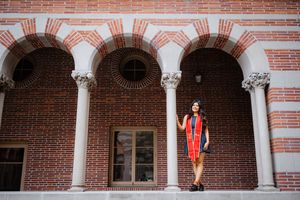 Graduate in orange regalia stands in front of brick archways during commencement ceremony at USC.
