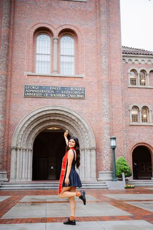 Graduate poses in front of ornate brick archway entrance at USC's historic campus Bovard building during graduation celebration.