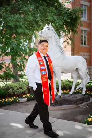 USC graduate in white shirt and red Class of 2026 stole poses confidently beside a white horse statue on campus.