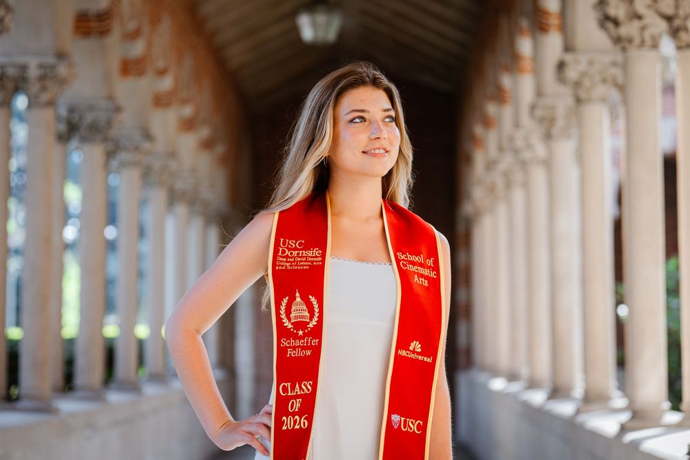 USC graduate in red and gold stole poses for photos in a beautiful outdoor colonnade setting.