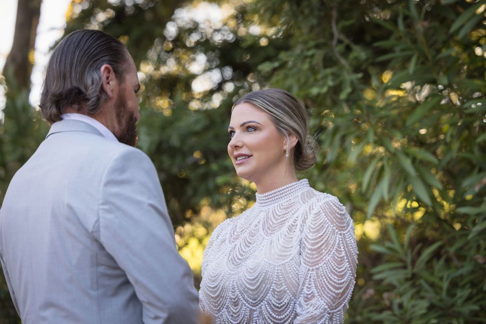 A bride and groom share an intimate moment outdoors surrounded by greenery during their wedding day.