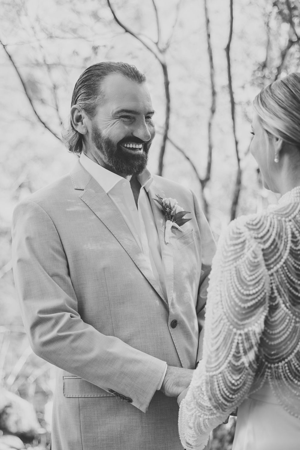 A black and white wedding portrait capturing a joyful moment between newlyweds in an outdoor setting.