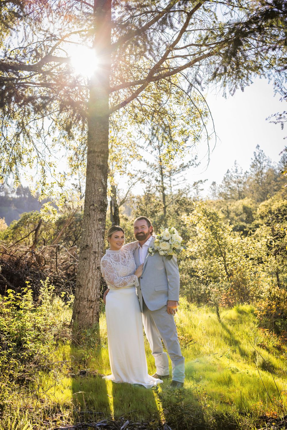 Sun-drenched outdoor photo session in a grassy field with pine trees creating a warm golden glow.