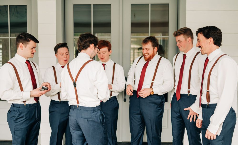 Groomsmen in white shirts and red ties share laughs and casual moments during wedding party preparations.