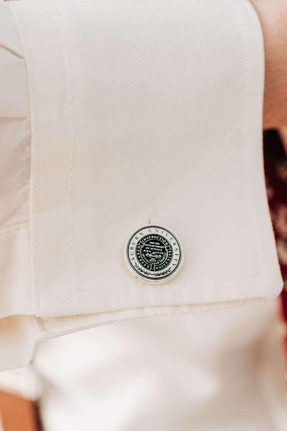 Close-up view of a white shirt cuff with a small green embroidered logo patch.
