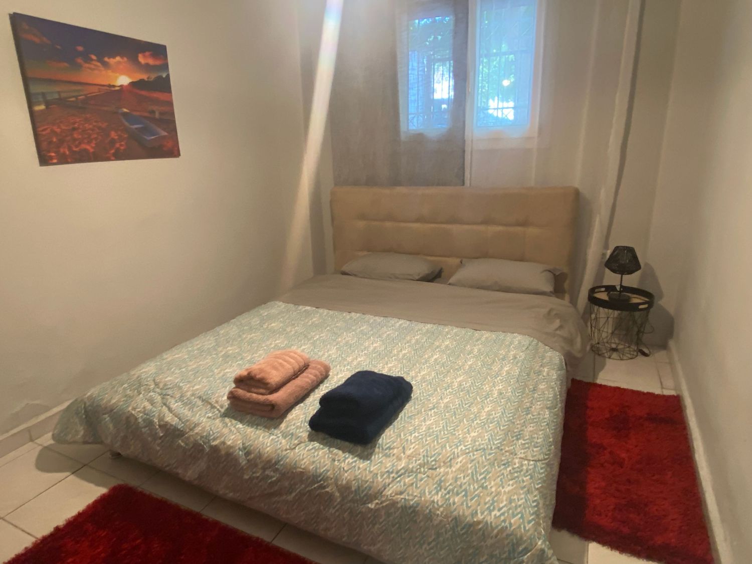 A bedroom interior with white walls featuring a bed with light blue bedding and red accents.