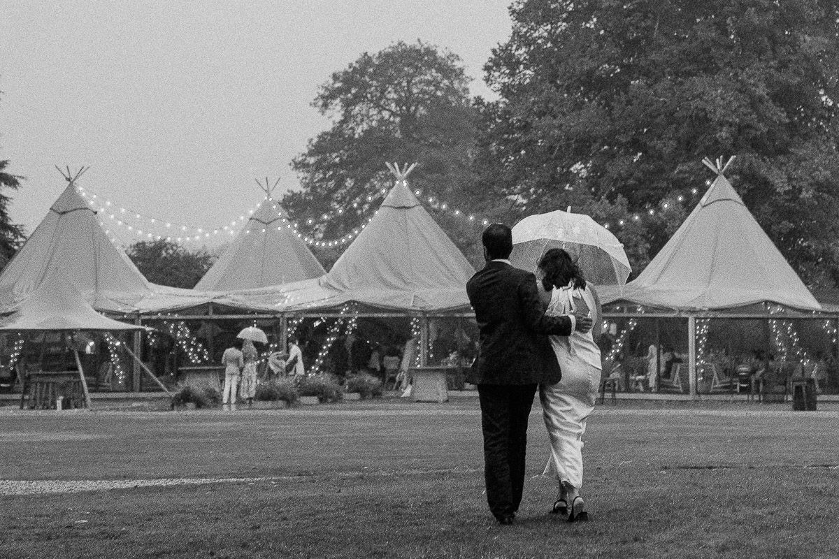 A row of white teepee tents set up in a grassy field with trees visible in the background.