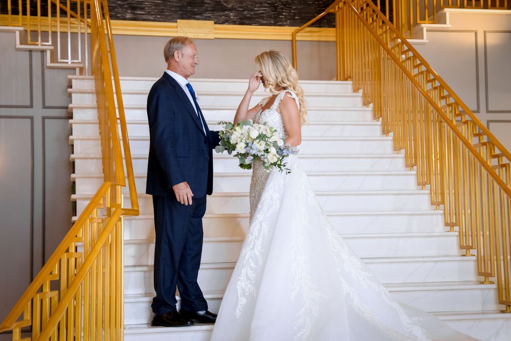 Wedding couple standing on elegant white staircase with gold railings during formal portrait session.