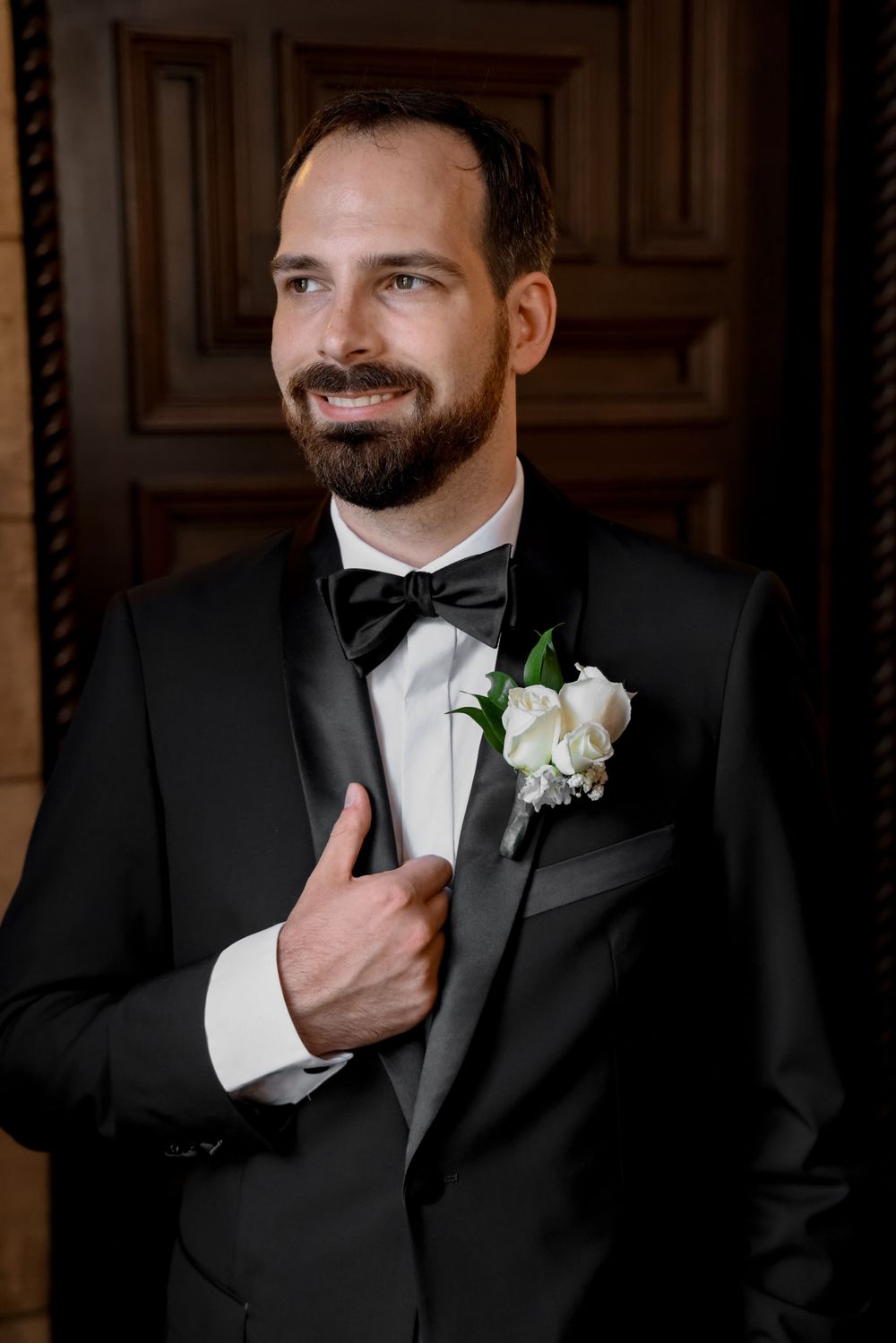 Groom in classic black tuxedo with white boutonniere poses in formal wedding portrait.