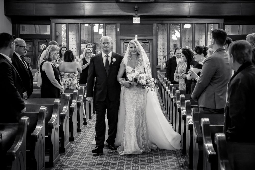 Black and white photo of wedding ceremony processional in traditional church setting.