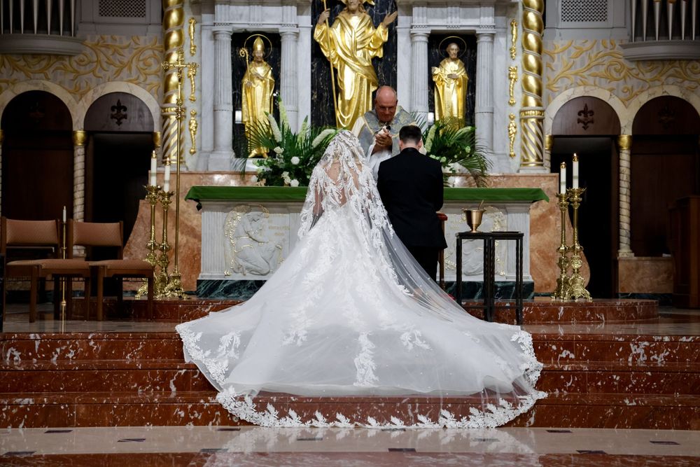 Dramatic back view of wedding couple at church altar with intricate lace train details.